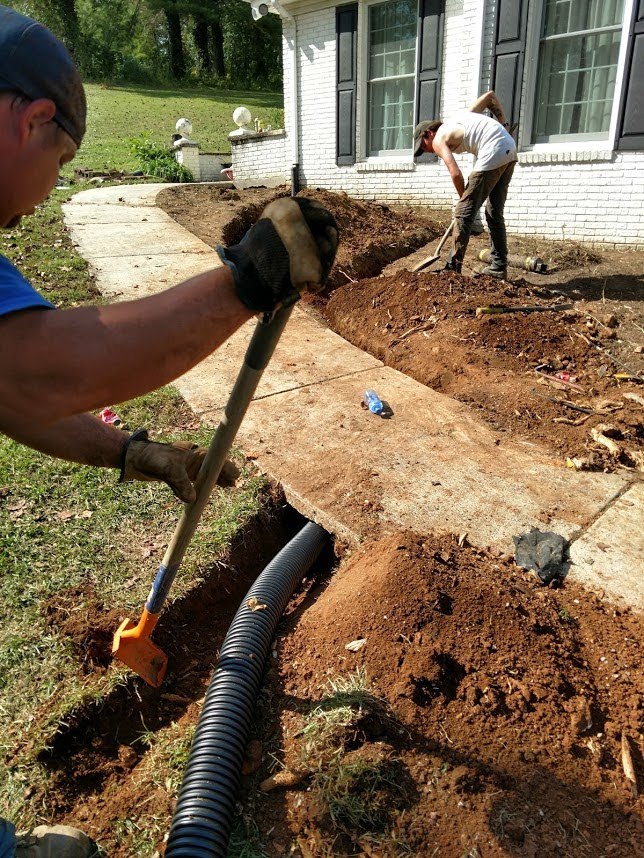 men digging a ditch near a house and sidewalk