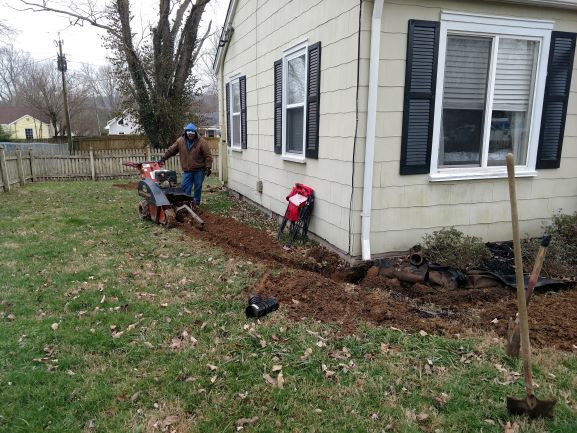man using machine to dig a ditch near a house